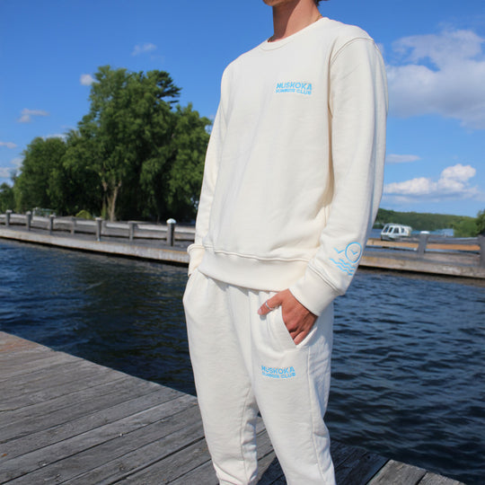 A person wearing a white sweatshirt and pants with branding by the lake.