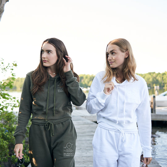 Two women in athletic wear standing by a lake with trees in the background