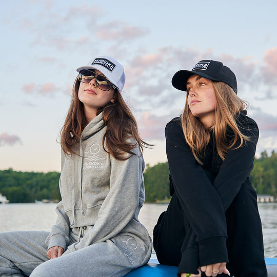 Two people sitting by a lake wearing branded caps and sunglasses.