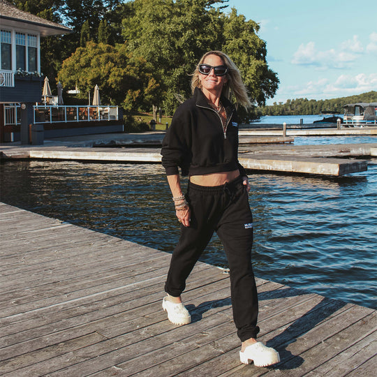 Person walking on a wooden dock by a lake, wearing black athletic wear.