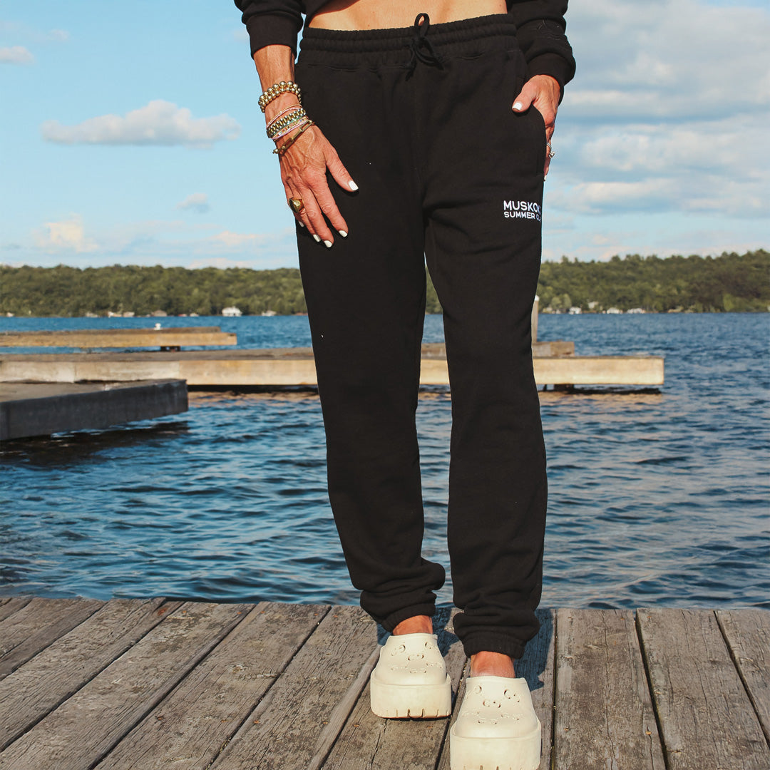 Person wearing black sweatpants with a logo by a lake