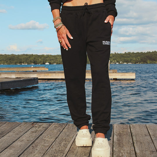 Person wearing black sweatpants with a logo by a lake