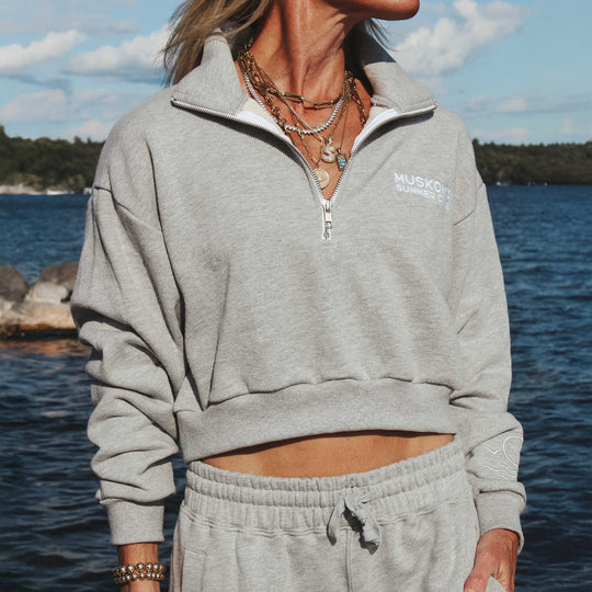 Person wearing a gray sweatshirt with a logo by the lake.