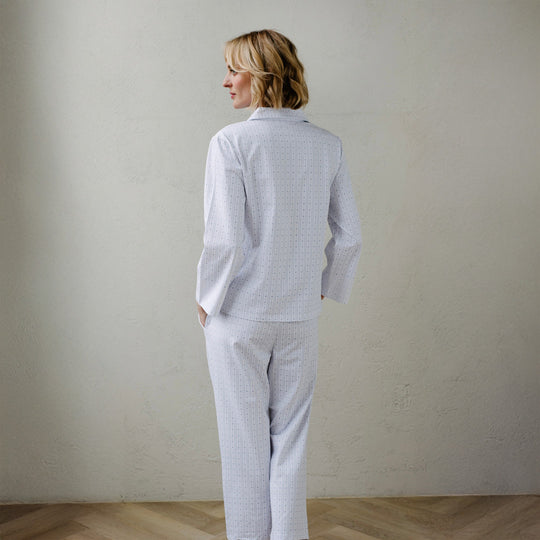 Woman wearing a light gray checkered pajama set against a plain wall.