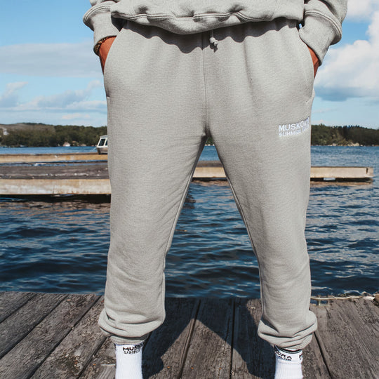 Person wearing gray sweatpants with a visible brand logo, standing on a wooden dock by the water.