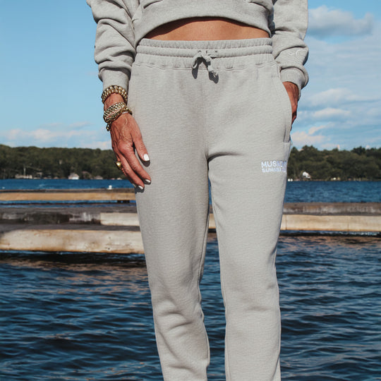 Person wearing gray sweatpants with a visible brand logo by a lakeside.