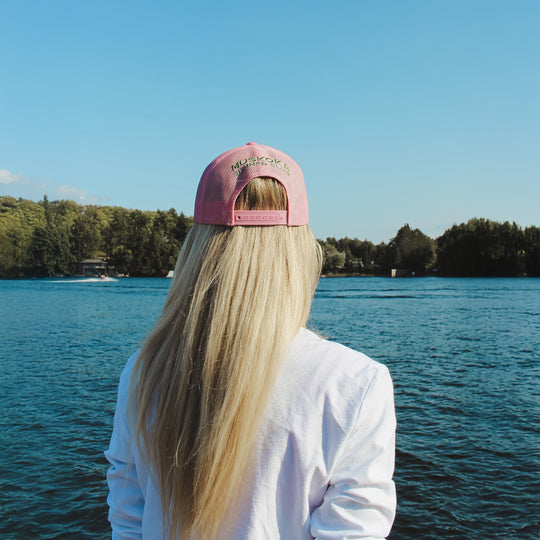 Person wearing a pink cap and white shirt standing by a lake with trees in the background