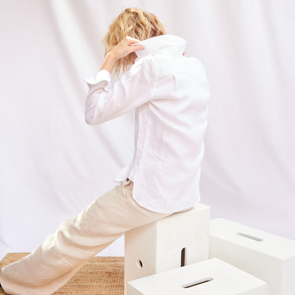 Person wearing a white shirt and beige pants sitting on a white box against a plain background