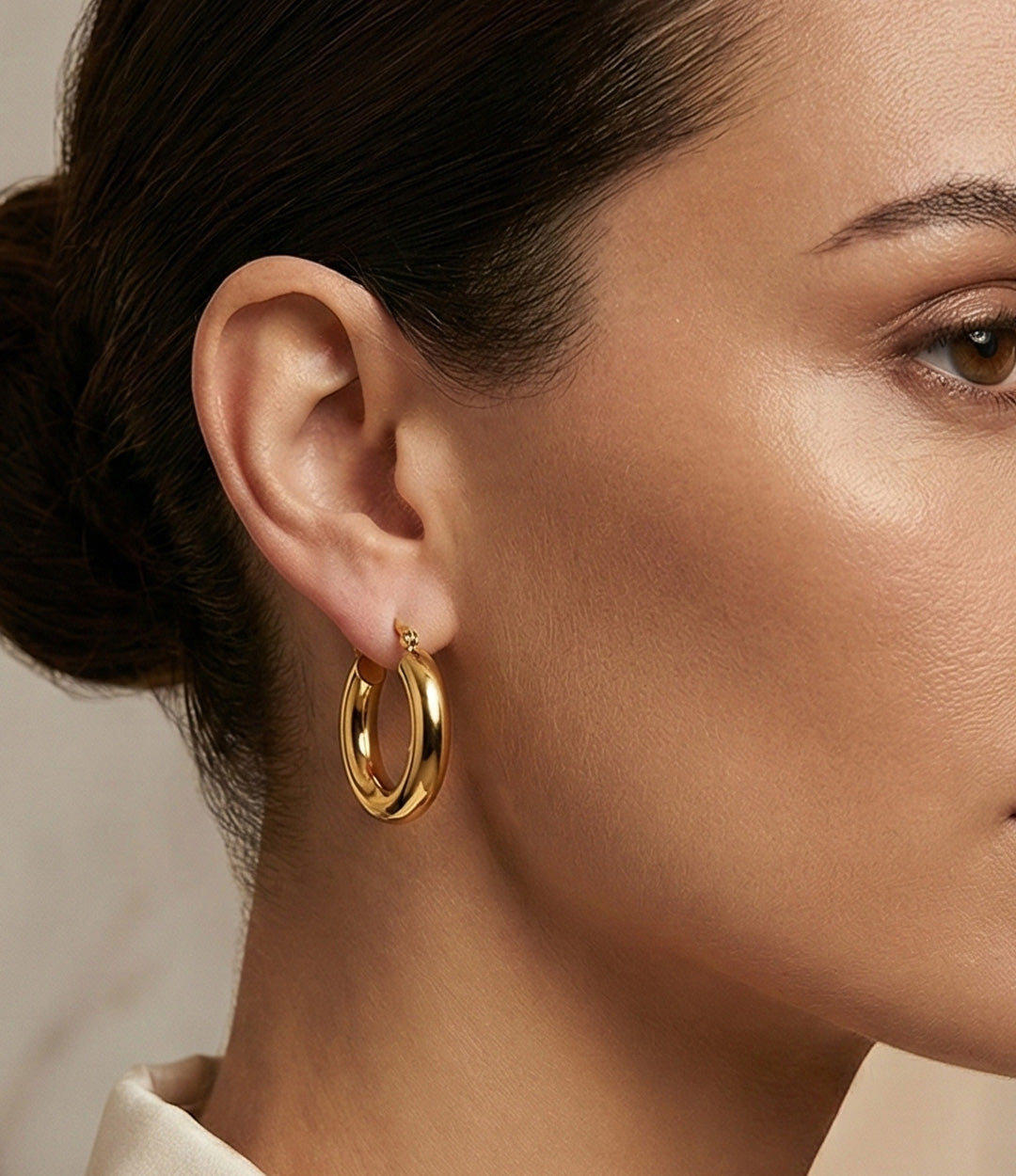 Close-up of a person wearing gold hoop earrings with a neutral background