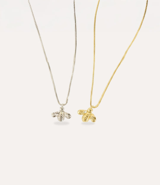 18K gold and silver Baby Bee Necklace displayed on a background with warm tones.