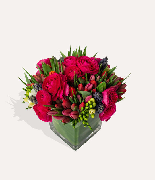 Bouquet of red and pink flowers in a clear vase on a light gray background