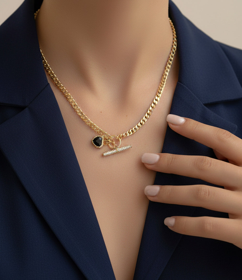 Gold necklace with a heart pendant and tag on a mannequin wearing a navy blazer.