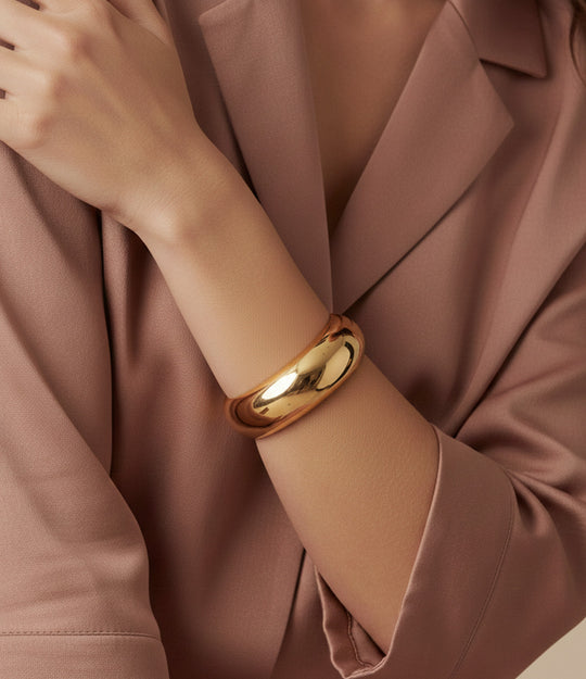 A classic gold bracelet on a person's wrist with a blurred background