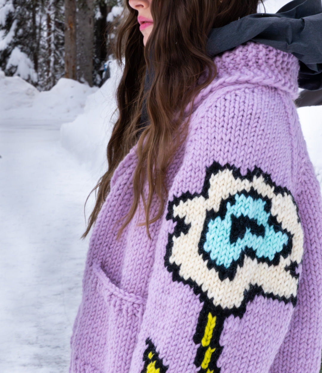 Person wearing a purple knitted cardigan with a colorful flower design in a snowy setting