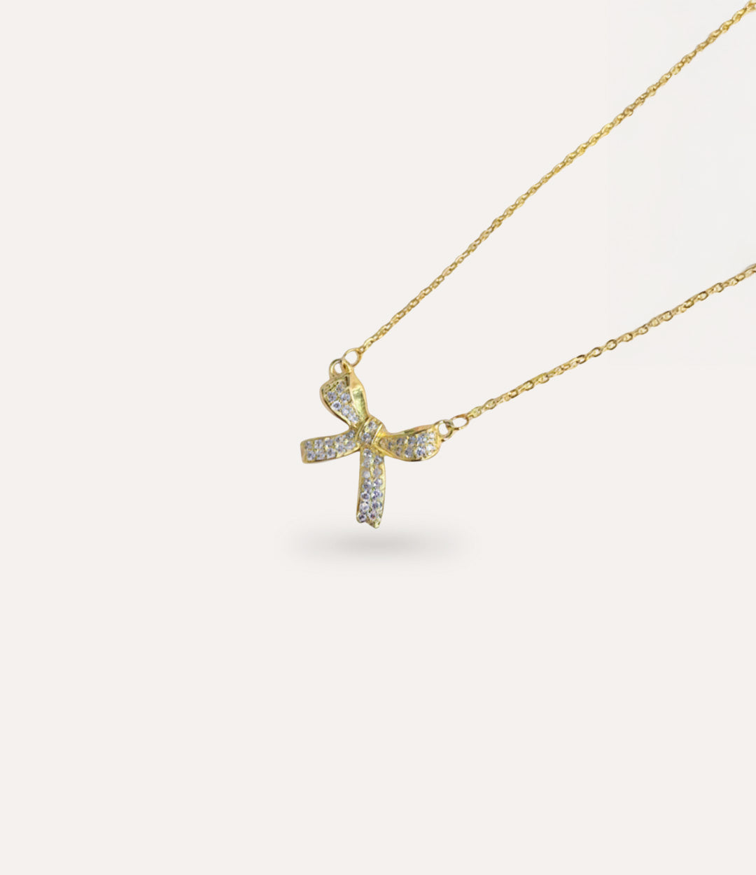 Gold necklace with a bow-shaped pendant on a light gray background