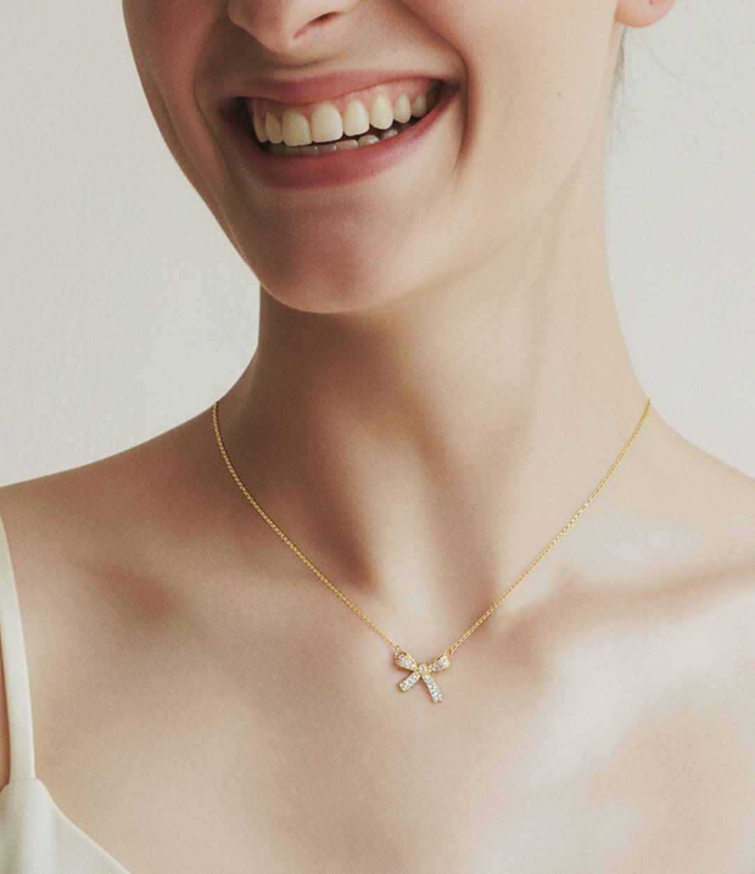 Woman wearing a gold necklace with a bow pendant on a plain background