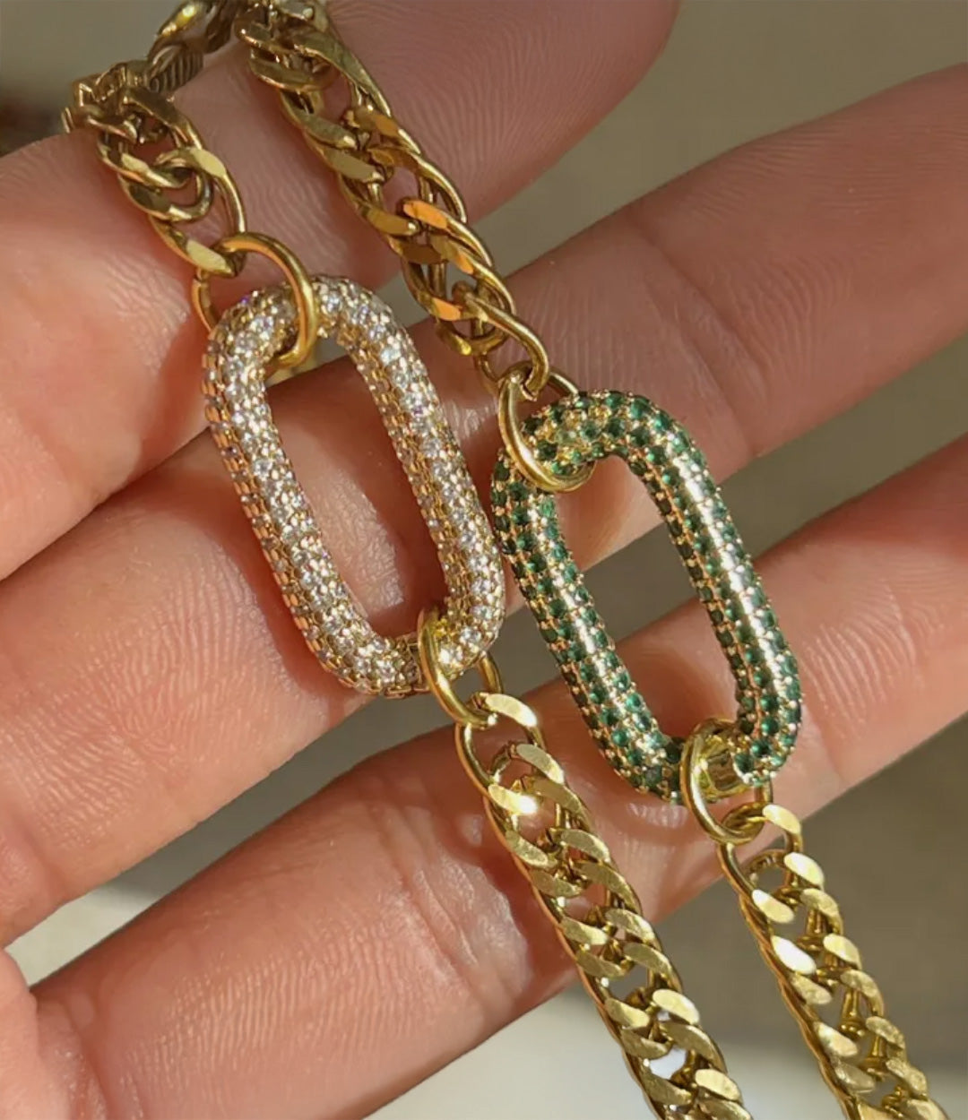 Gold chain with diamond and emerald-studded links held between fingers.