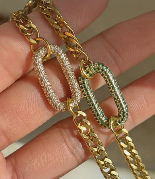 Gold chain with diamond and emerald-studded links held between fingers.