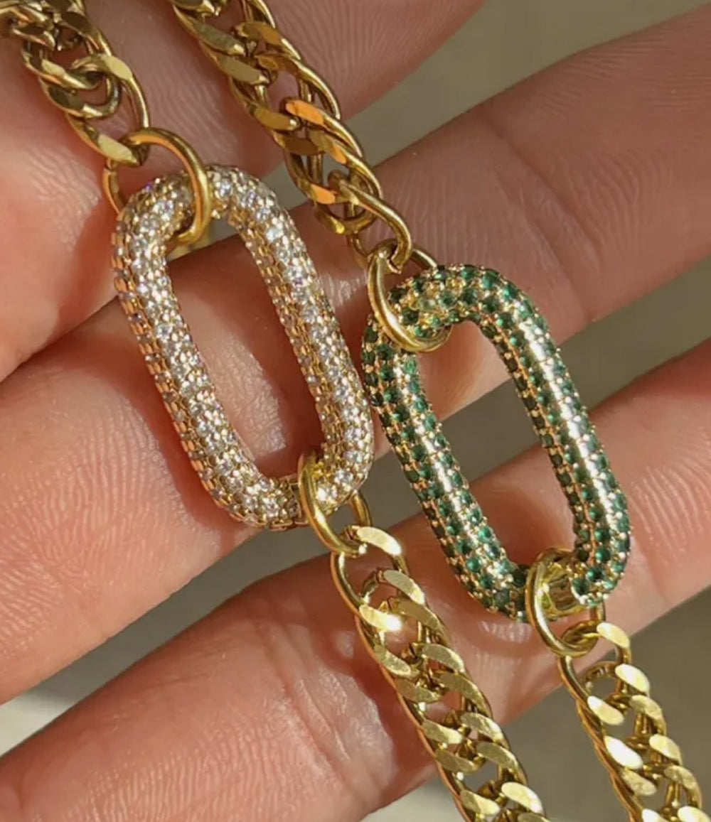 Gold chains with diamond and emerald accents held in a hand.