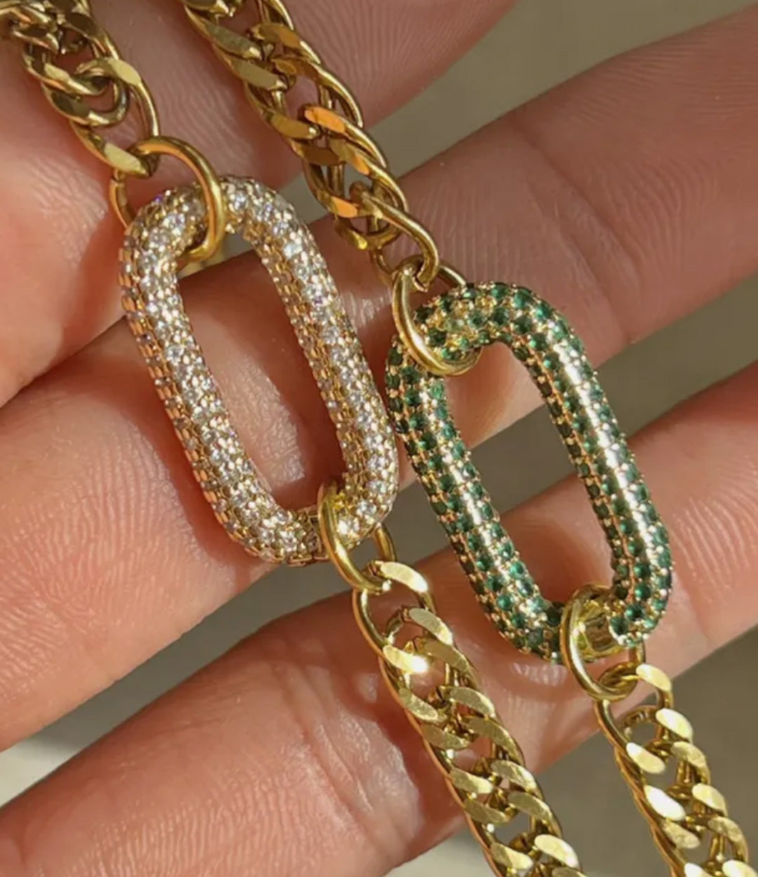 Gold chains with diamond and emerald accents held in a hand.
