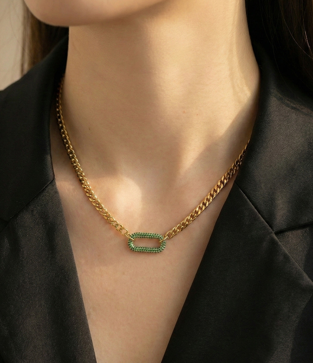Gold chain necklace with green gemstones worn by a person against a black background