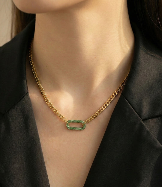 Gold chain necklace with green gemstones worn by a person against a black background