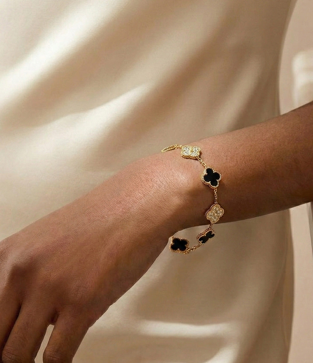 Gold bracelet with black clover charms on a person's wrist against a beige background