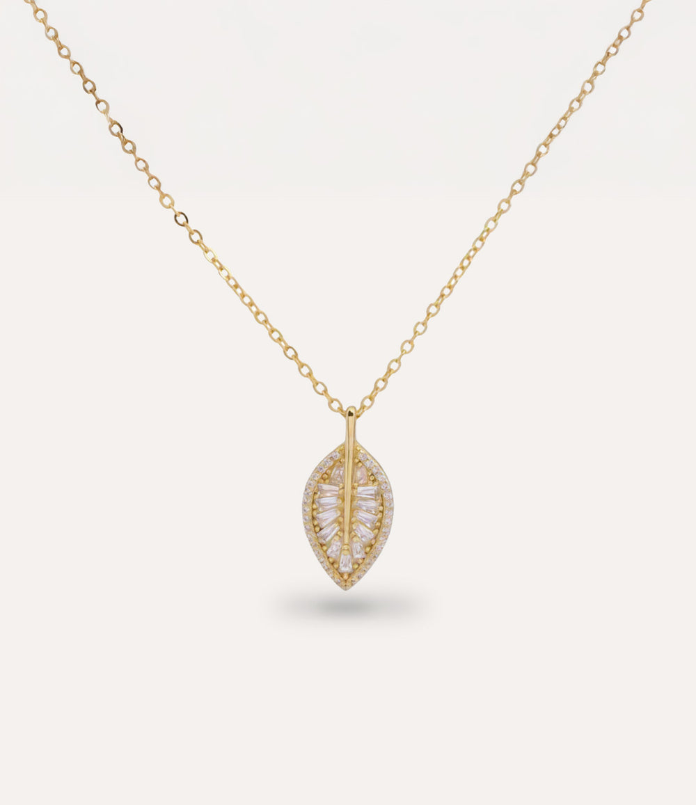 Gold necklace with a leaf-shaped pendant with sparkling diamonds on a light gray background