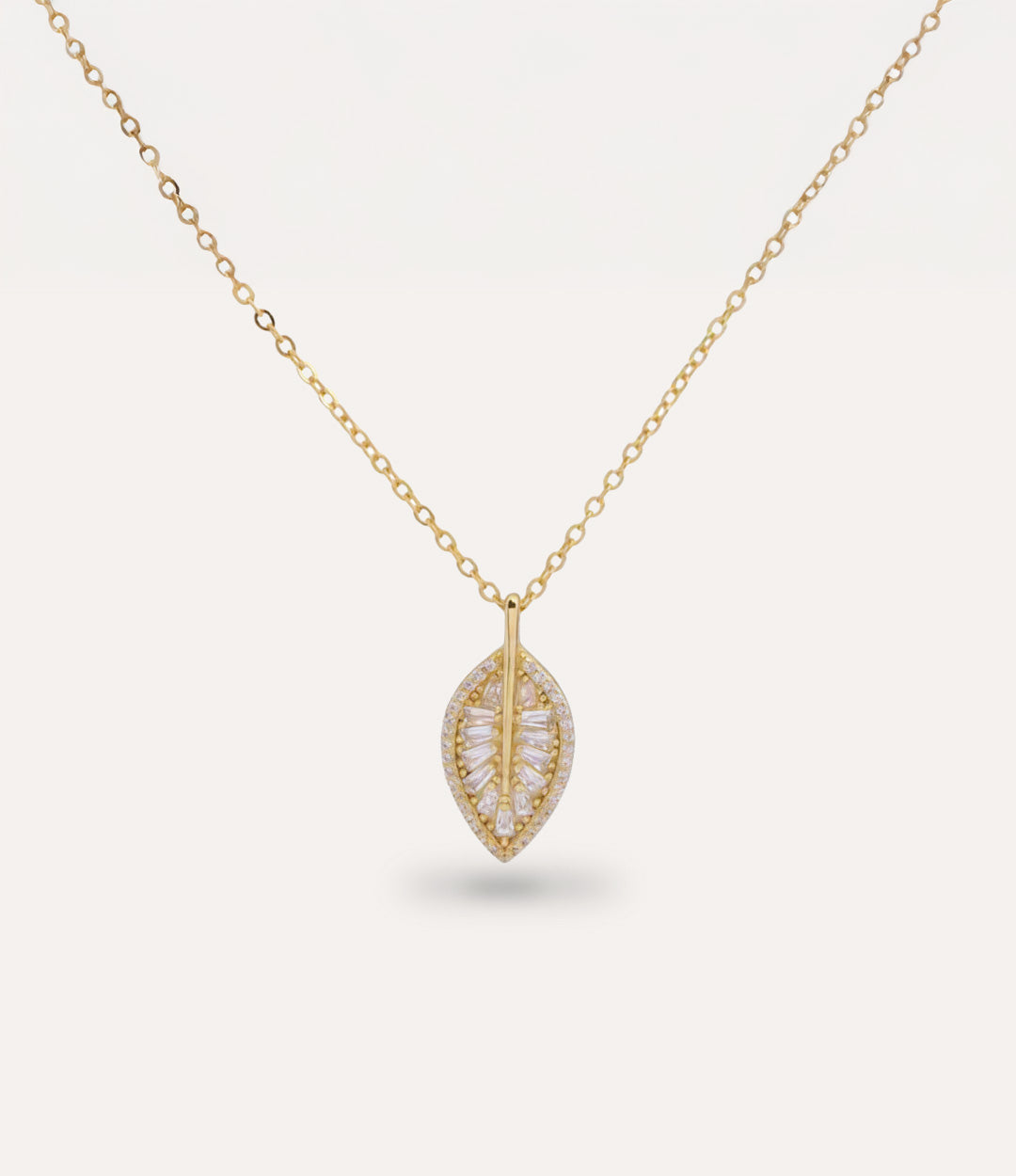 Gold necklace with a leaf-shaped pendant with sparkling diamonds on a light gray background