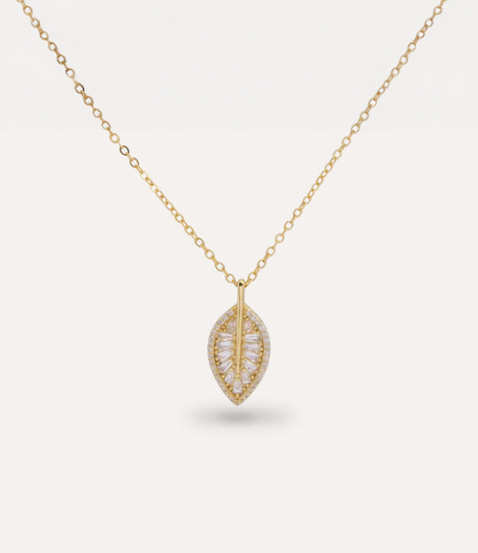 Gold necklace with a leaf-shaped pendant with sparkling diamonds on a light gray background