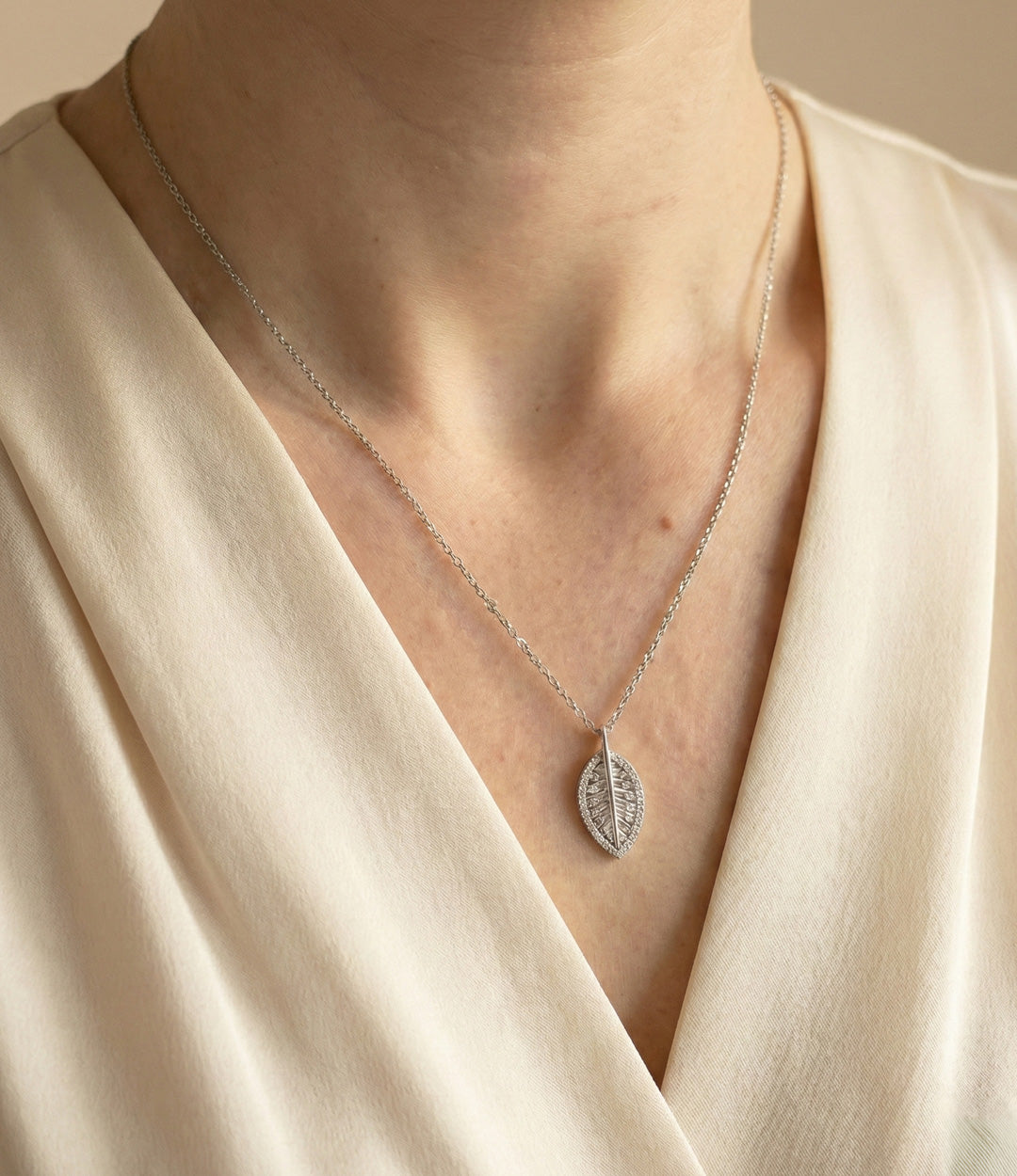 Silver necklace with a leaf pendant worn by a person in a beige top.