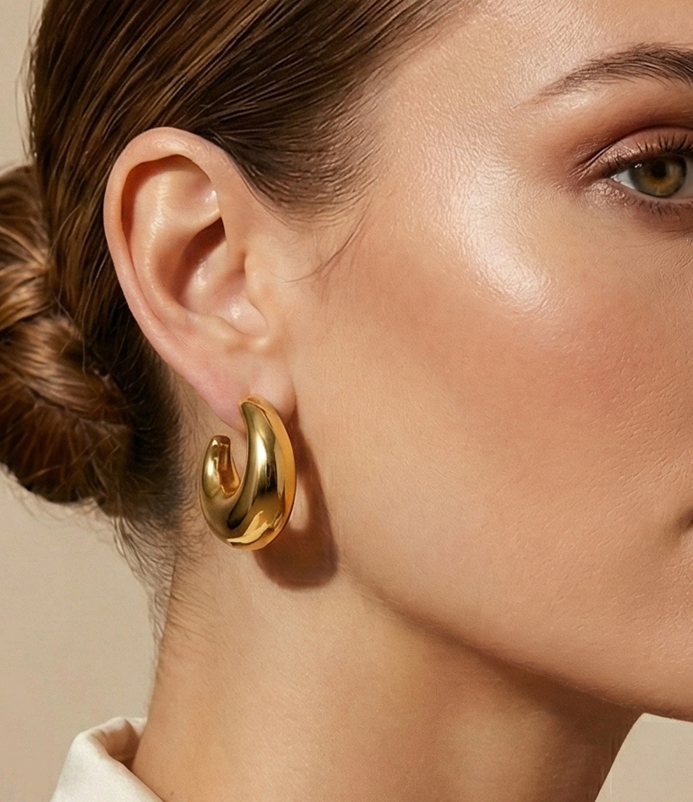 Close-up of a woman wearing gold hoop earrings with a neutral background