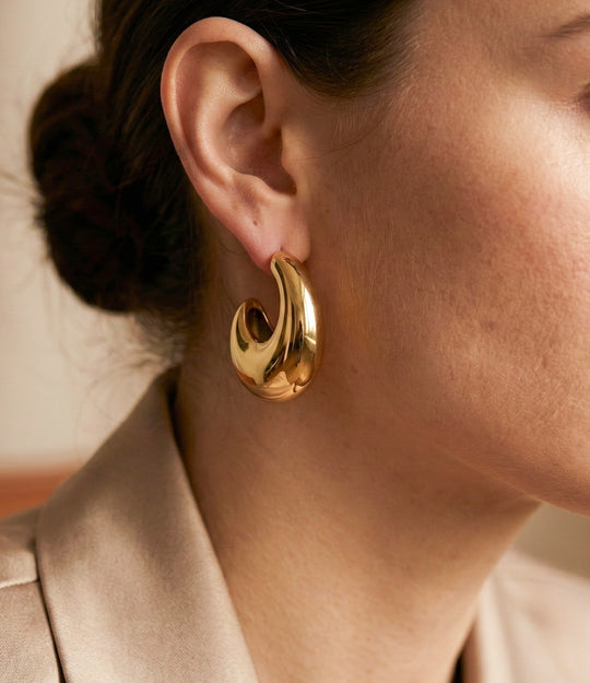 Gold hoop earring worn by a person with a neutral background