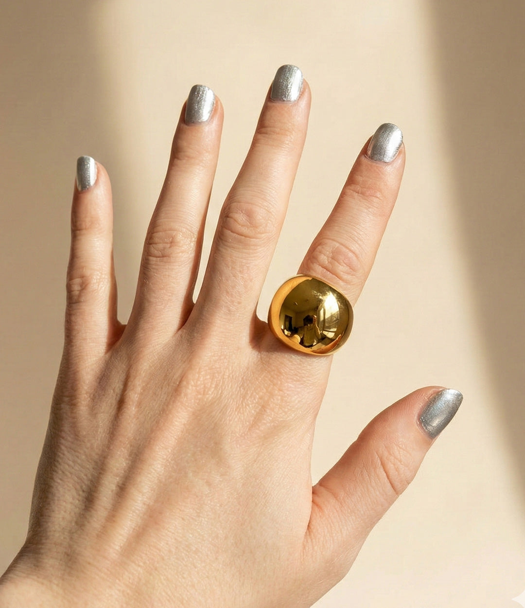Hand wearing a gold ring with a beige background