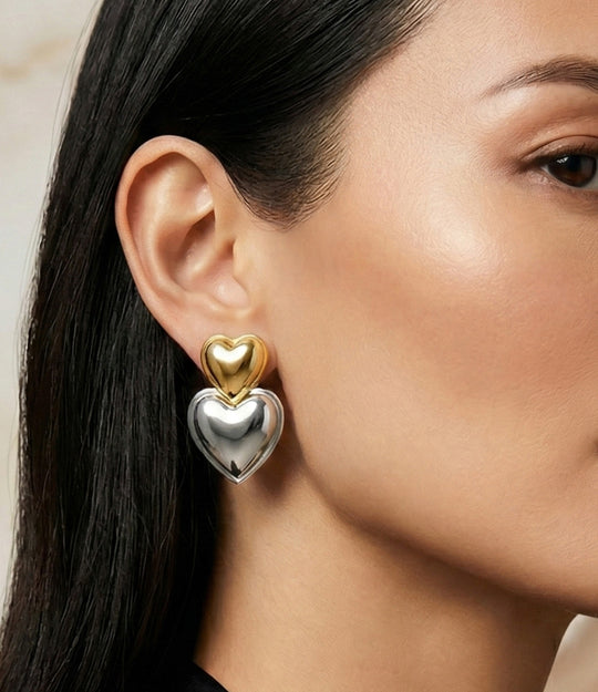Close-up of a person wearing a gold and silver heart-shaped earring.