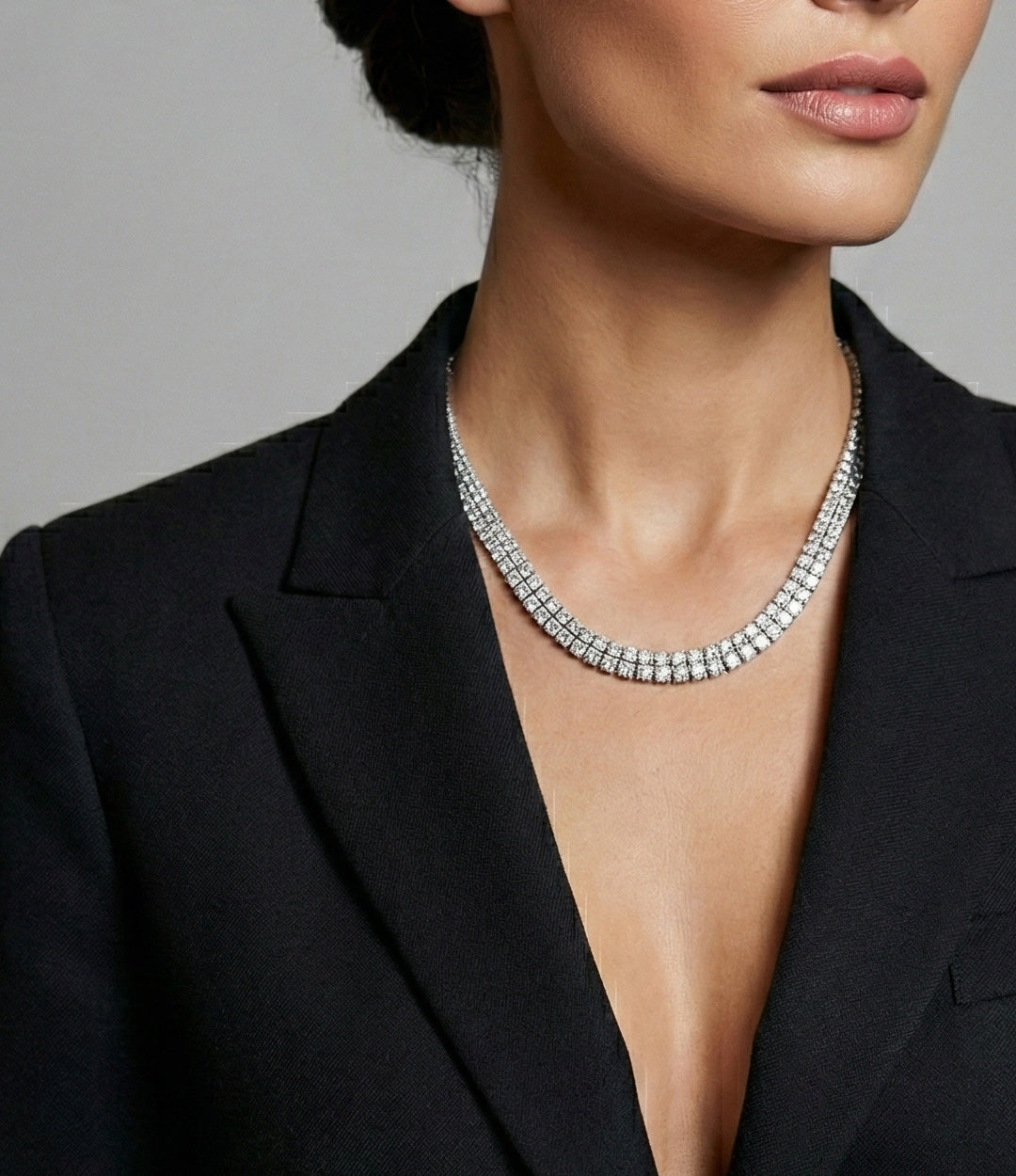 Woman wearing a sparkling necklace with a black blazer against a gray background