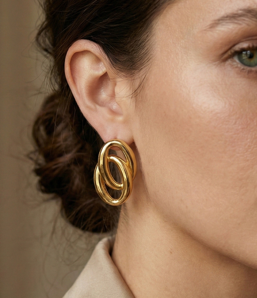 Close-up of a woman wearing gold hoop earrings with a neutral background