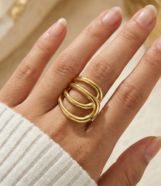 Woman's hand modeling the Double Loop Ring on the middle finger, showcasing the bold architectural shape and sophisticated gold shine.