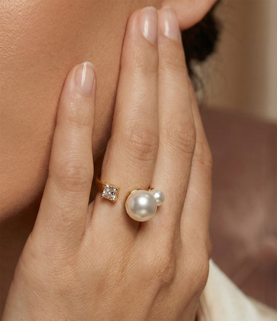 Woman's hand modeling the Double Pearl Ring alone on the ring finger, showcasing the two lustrous pearls and chic gold design against a soft neutral background.