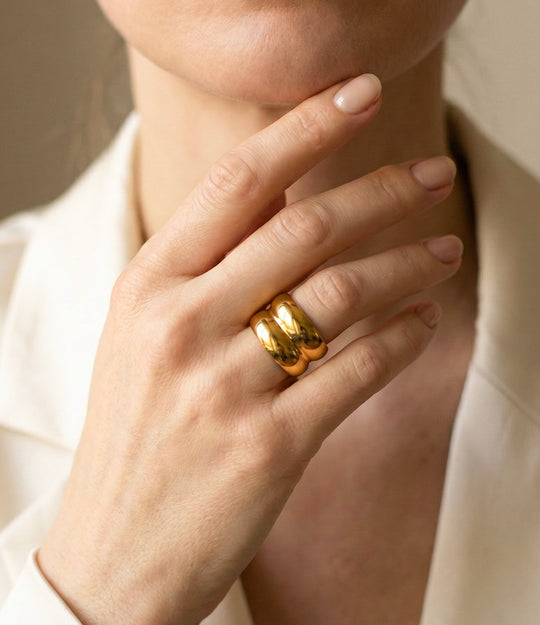 Close-up of a hand wearing a gold ring with a neutral background
