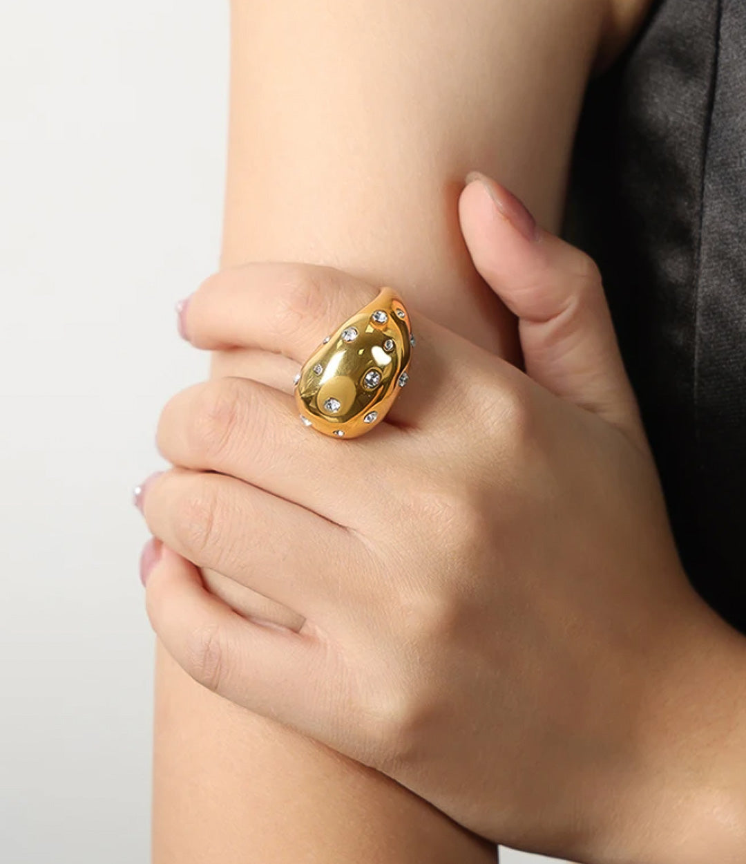 Woman's hand modeling the Drop Ring on the pointer finger, showcasing the unique arrangement of glistening stones and pearls against a gold band.