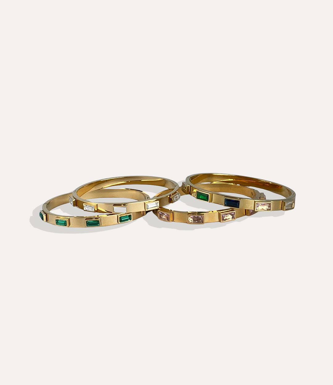 Three gold bangles with embedded gemstones on a white background