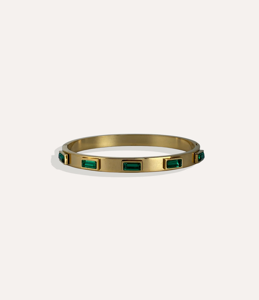 Gold bracelet with emerald green stones on a white background