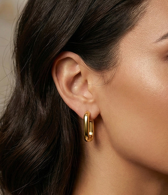 Close-up of a person wearing a gold hoop earring with a neutral background