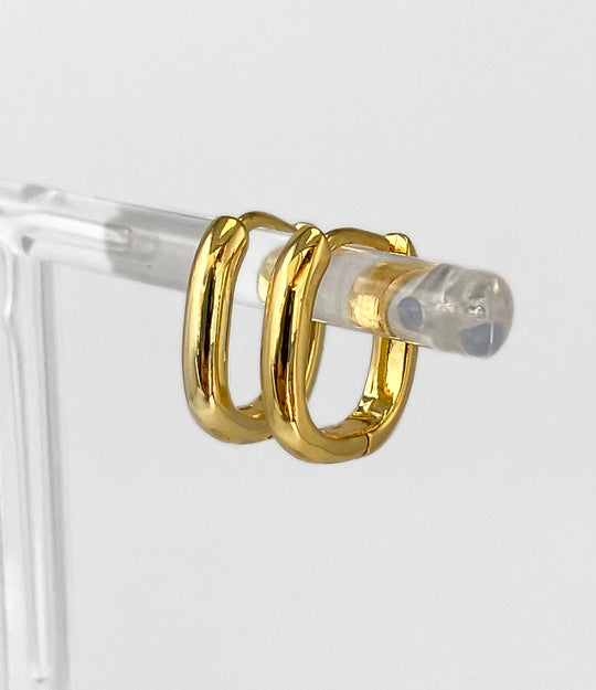 Gold hoop earrings on a clear stand against a light gray background