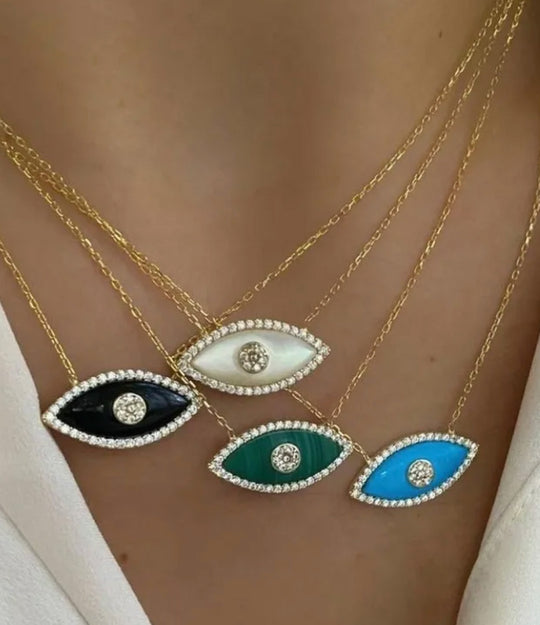 Four gold necklaces with eye-shaped pendants in black, white, green, and blue on a blurred background.