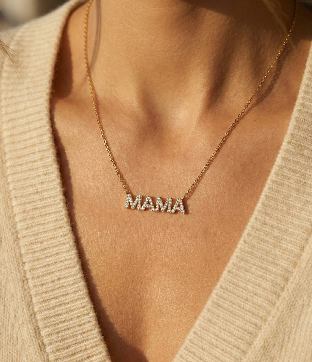 Necklace with 'MAMA' pendant worn by a person in a beige cardigan.