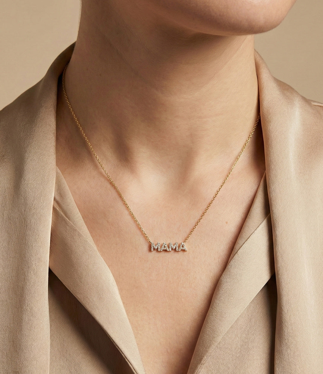 Necklace with 'MAMA' pendant worn by a person in a beige outfit.