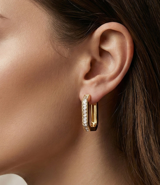 Close-up of a woman wearing gold hoop earrings with clear stones.