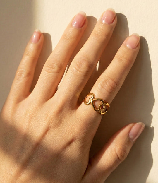 Model wearing Heart Link Ring in 18k gold-plated stainless steel, featuring a chain of connected heart shapes and an adjustable band, isolated on white.